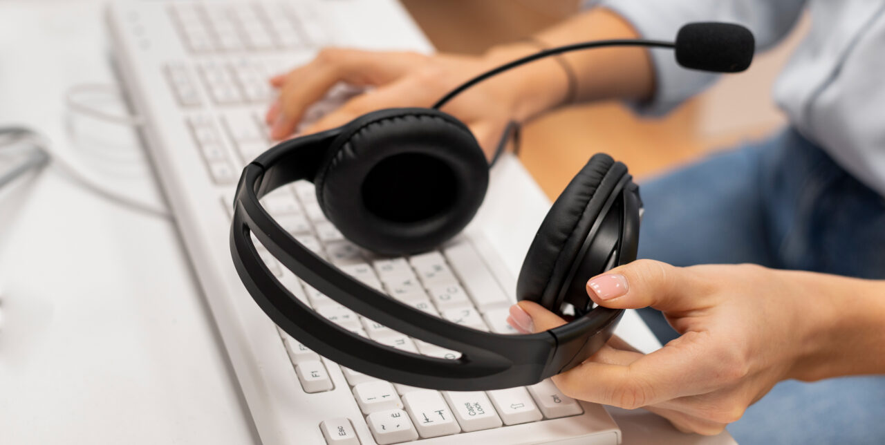 Hände halten ein Headset über einer Computertastatur